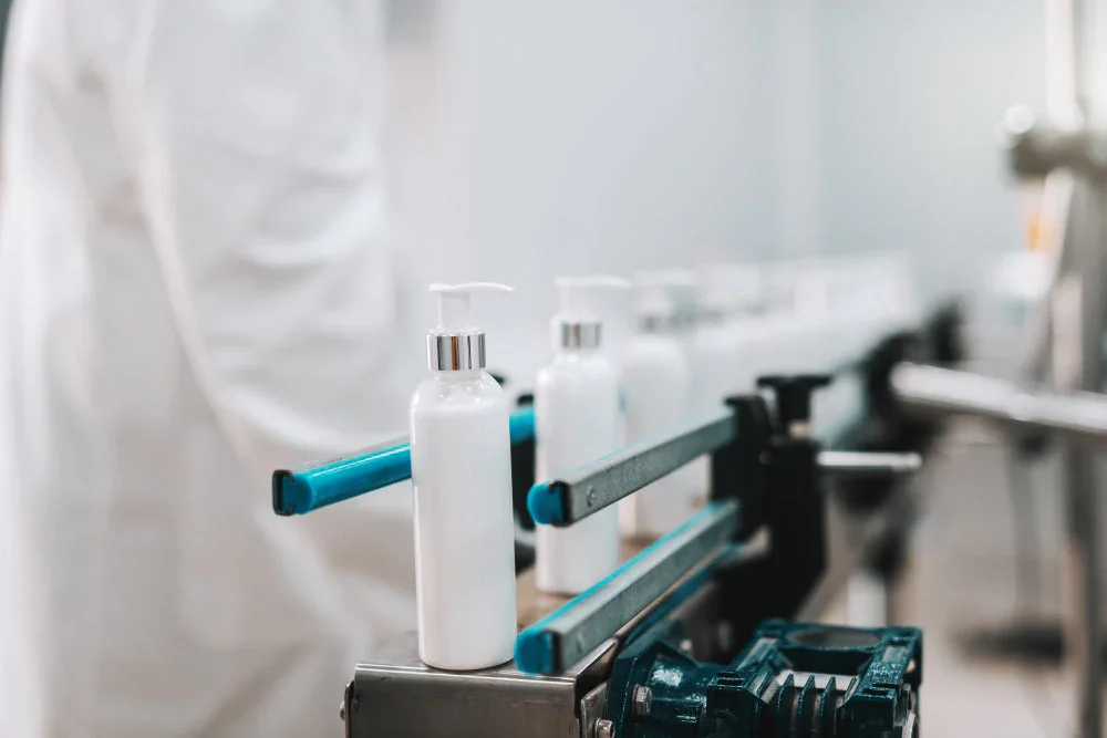 White bottles with pumps on an assembly line in a factory setting, indicating skincare product production.